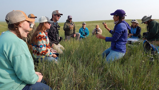 teacher lecturing to students sitting in a field