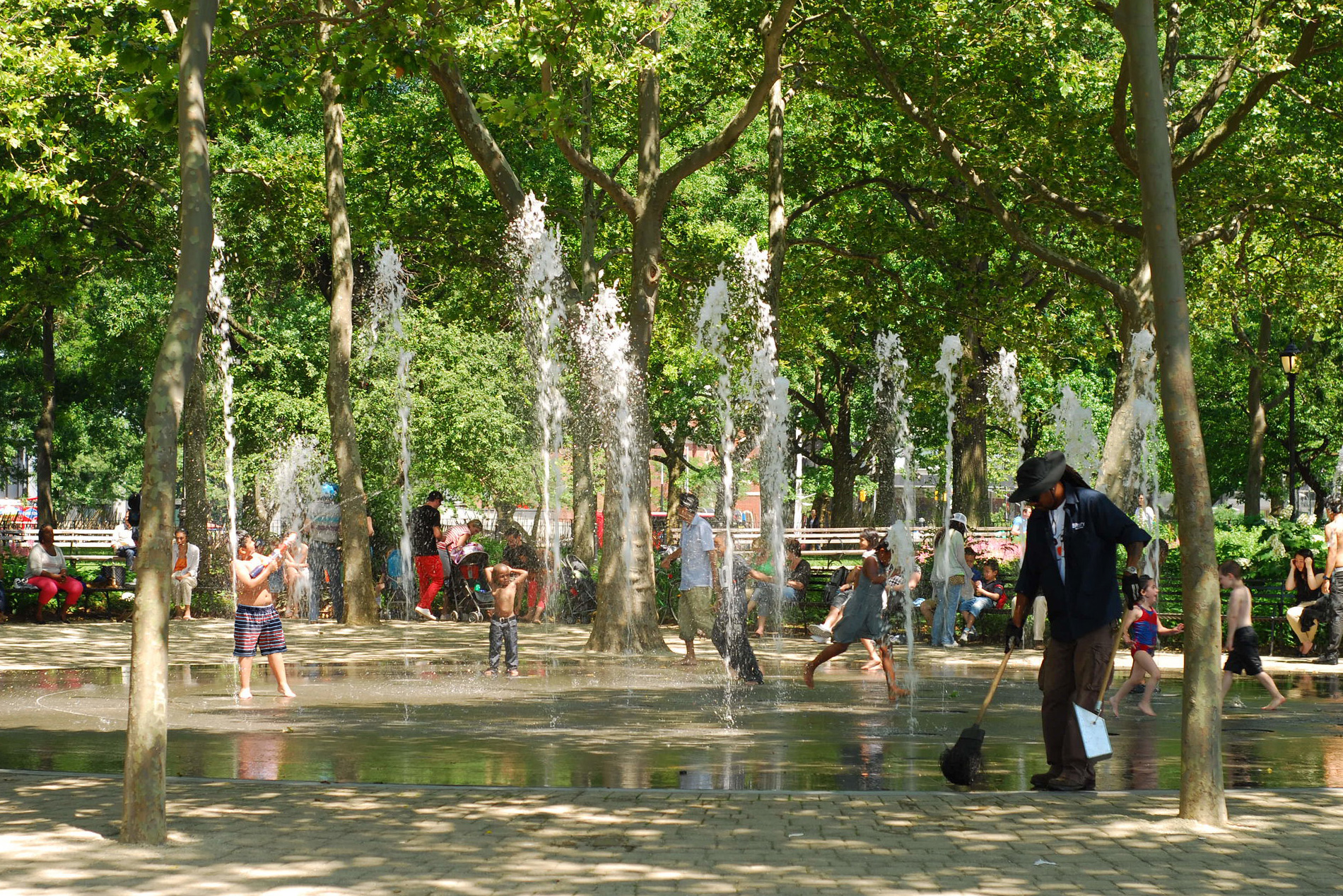 Kids play in a fountain in a tree-shaded park