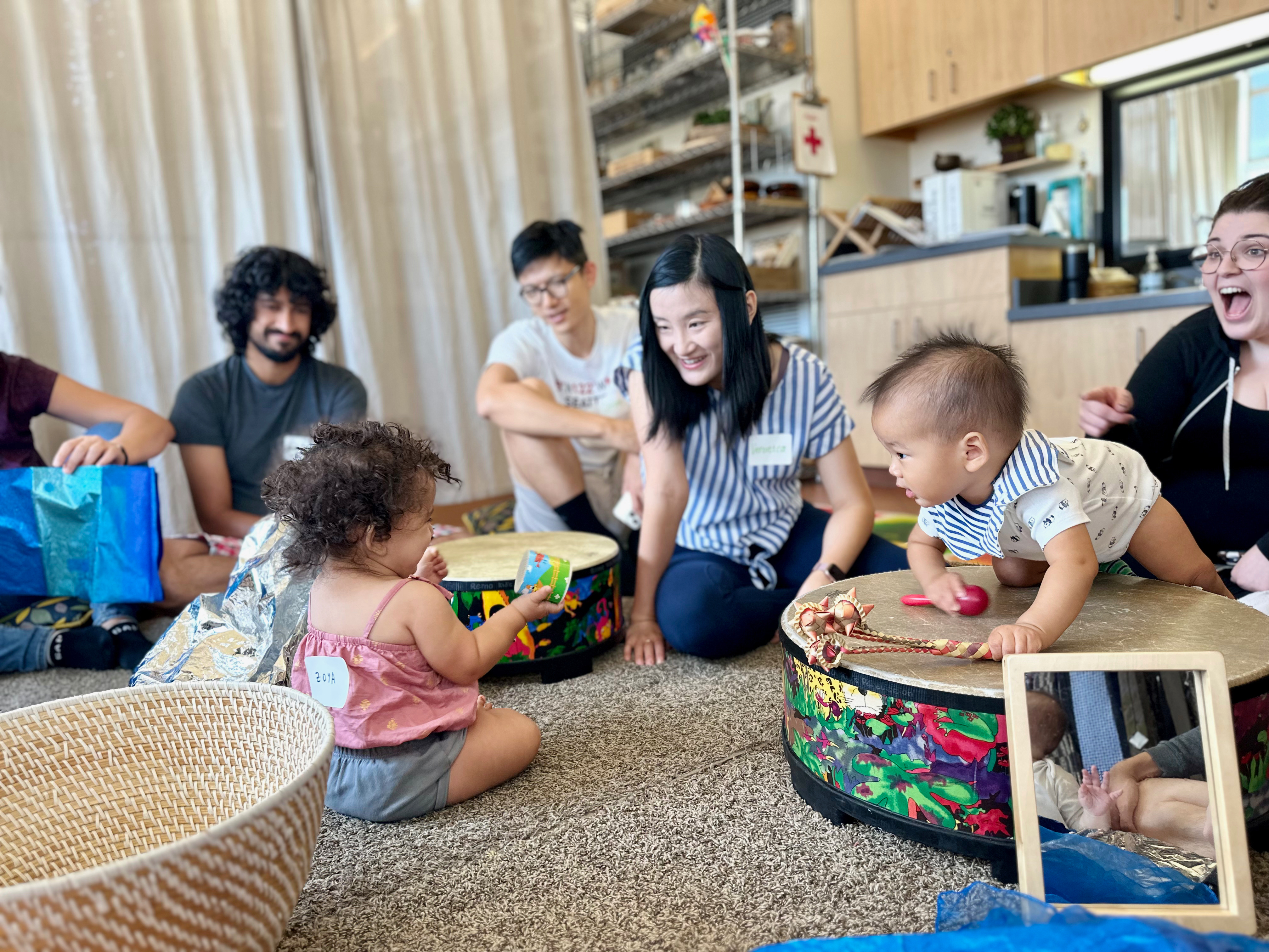 two infants greet each other with a smile as they climb over drums and other instruments.