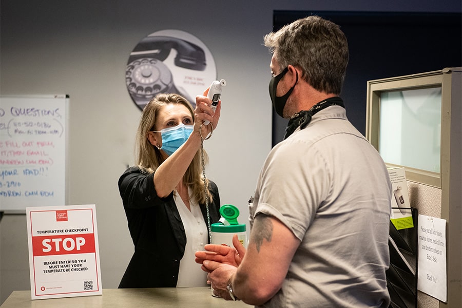 image of someone behind a counter checking the temperature of someone with a no-contact thermometer