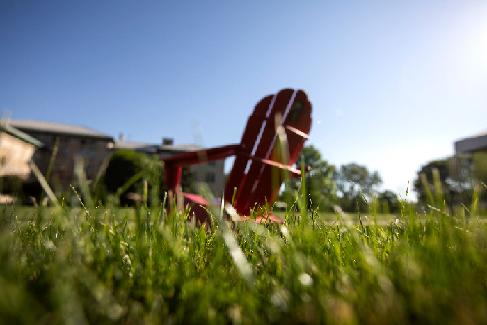 Red adirondack chair with grass in foreground and CMU building and blue sky in the background