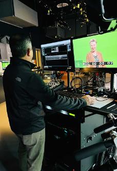 Dr. Hammond standing in front of a green screen being recorded by a camera man