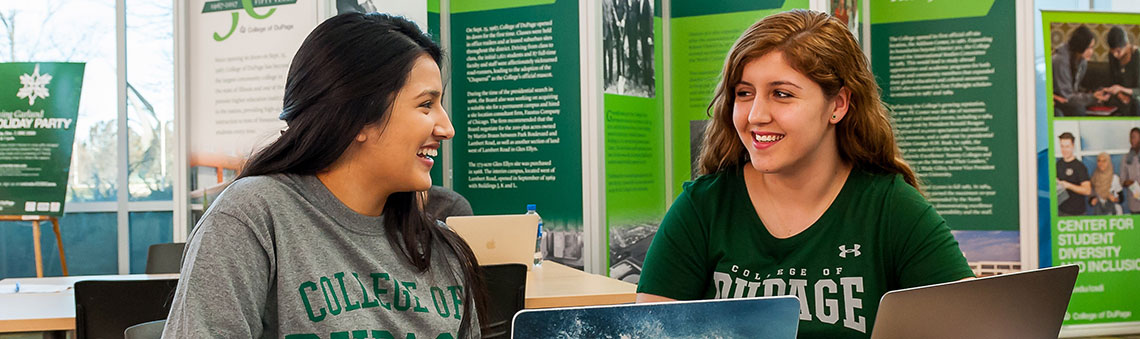 two students smiling at each other while working on computers