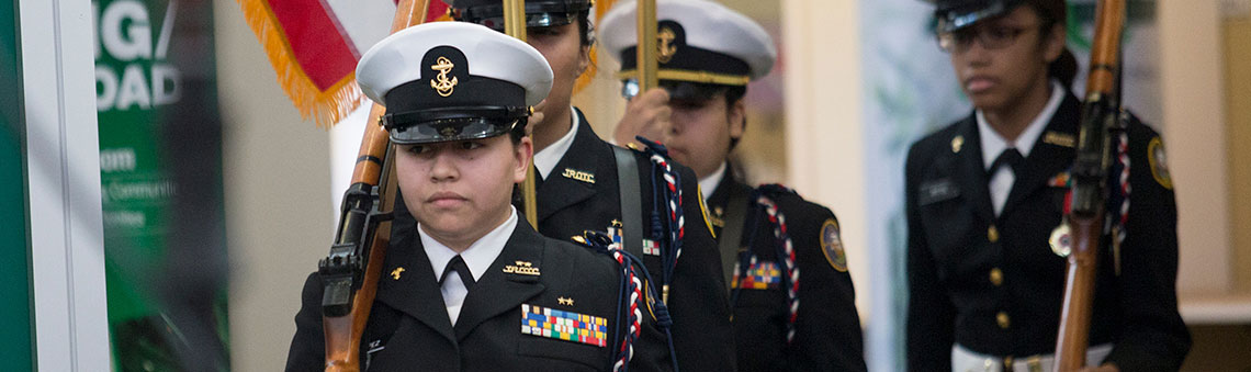 Students in military uniforms carrying rifles