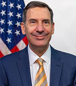 Headshot of Steve Brockelman. Steve has dark hair and a blue striped suit with a yellow tie.