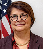 Headshot of Denise Maes. Denise has short brown hair and is wearing a red shirt and a maroon jacket.