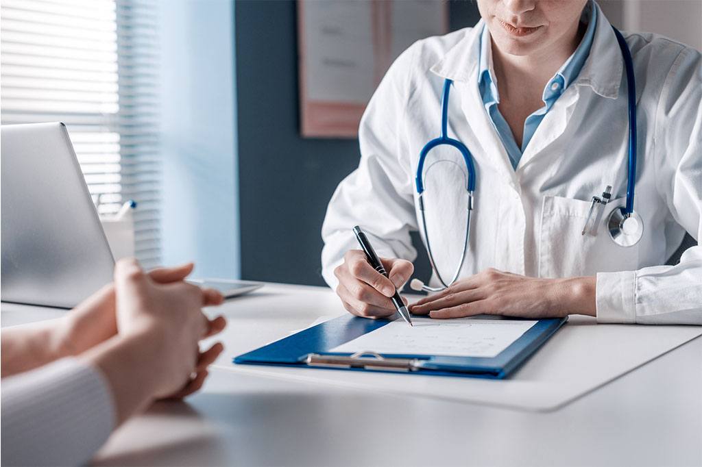 A doctor speaking with a patient takes notes on a notepad