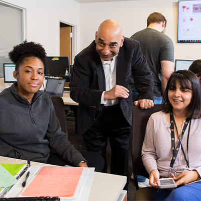 Students at desk with teacher assisting them