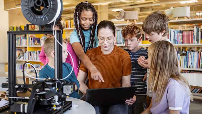 Six children and an adult using a 3D printer