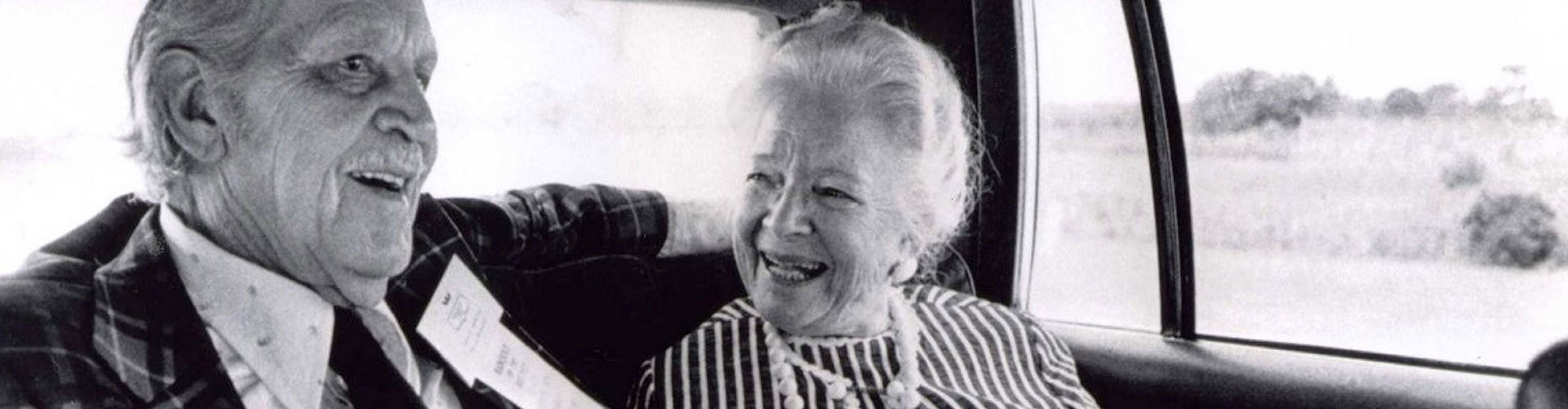 A black and white image of a man and women smiling and laughing in a car.