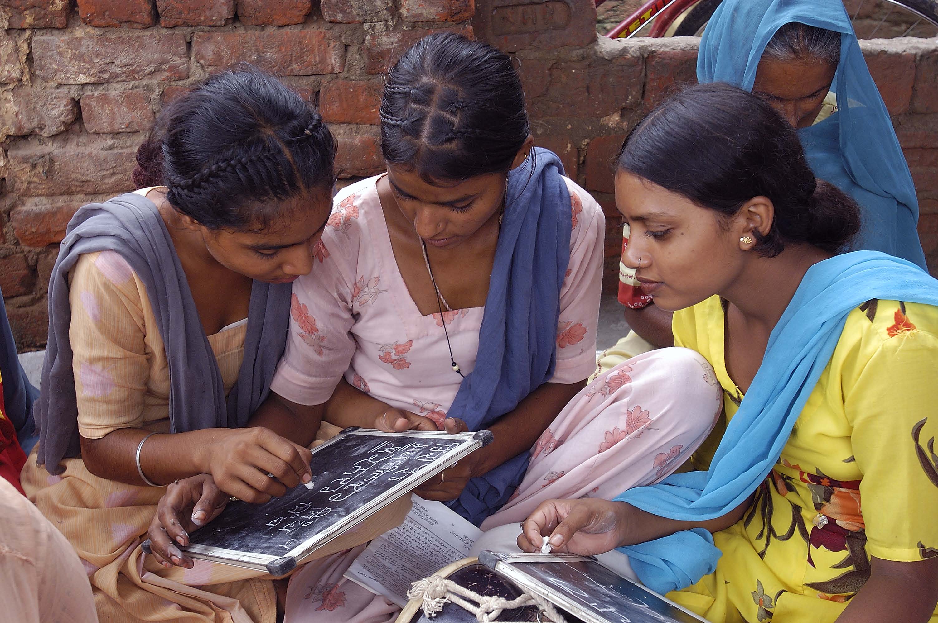 A group of women sit together while writing on a chalkboard.