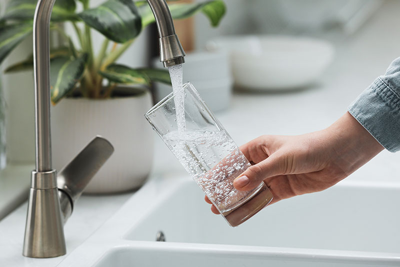 Hand holds glass being filled with water from tap.