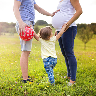 child reaching up toward man and preganant woman