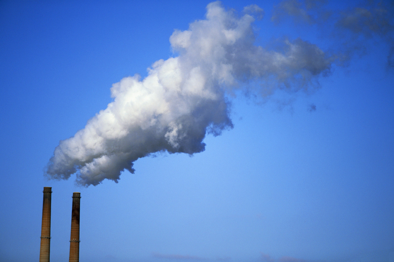 Two smoke stacks billowing smoke into a clear, blue sky 