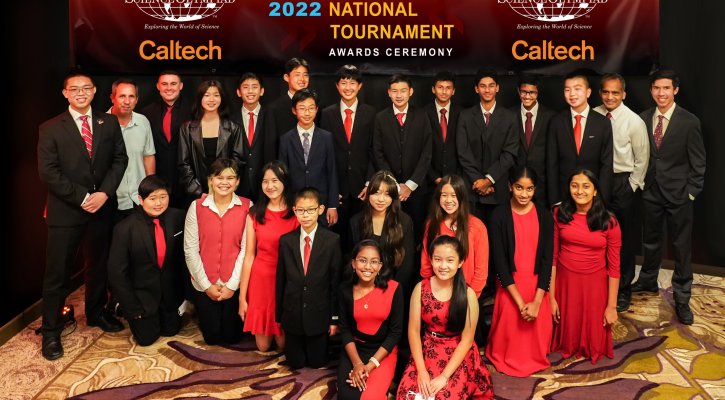 A group of students wearing their school colors (red and black) stand in front of a large Science Olympiad Caltech banner.