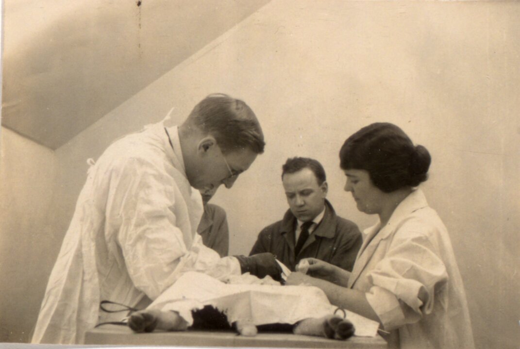 Original black and white photograph showing Banting, assisted by Sadie Gairns, performing surgery on a dog. Unidentified man in background.