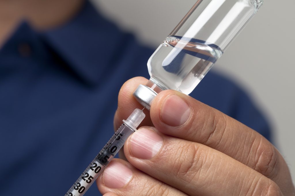 Male hands filling a syringe with the right dosage for an insulin shot. 