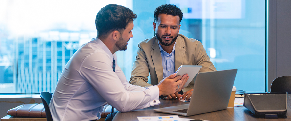 Two men looking at information on a laptop and tablet