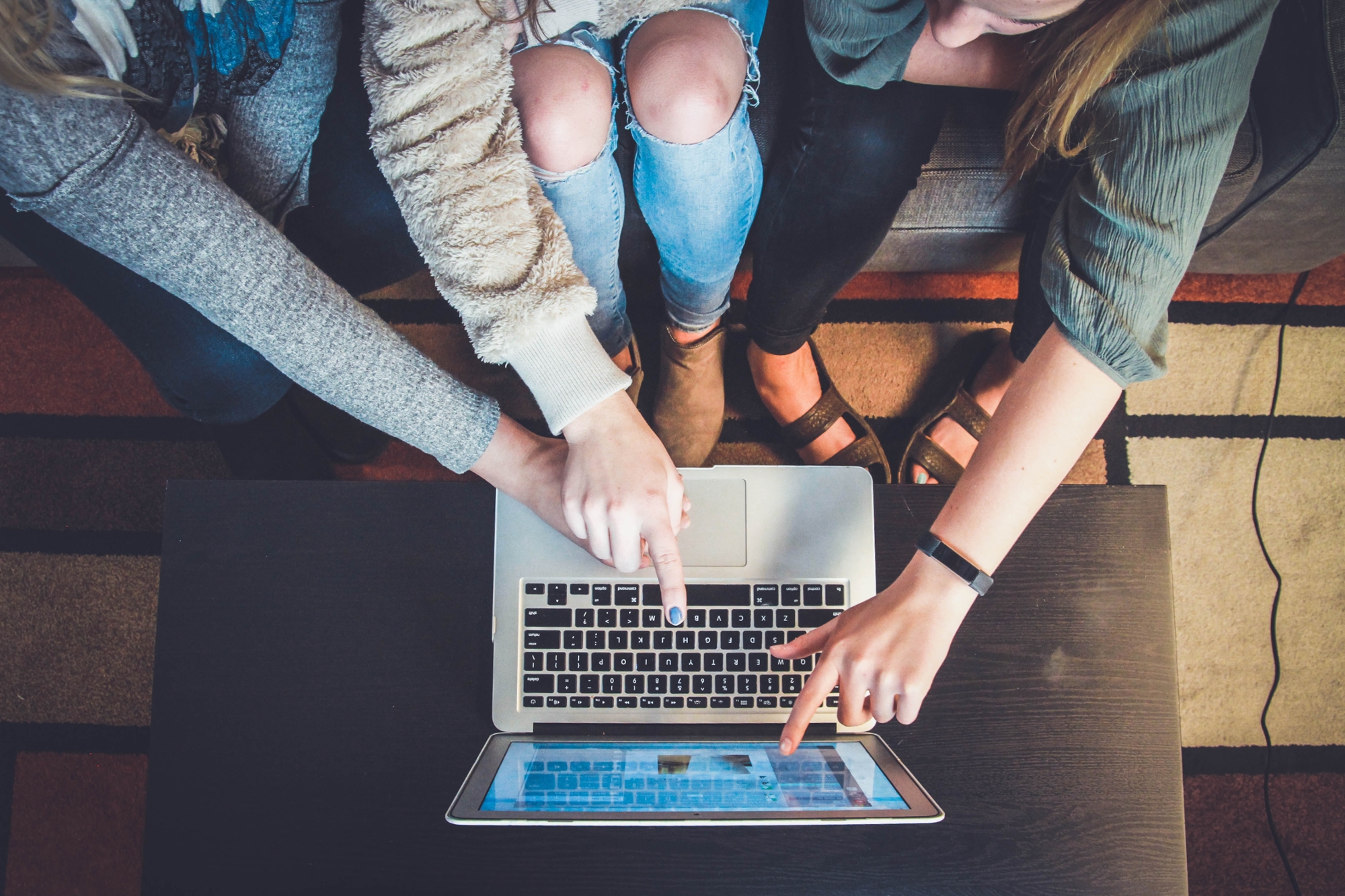 Pictured: three students work at a laptop together, pointing at the screen and making suggestions