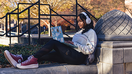 A Purdue student sitting outside with a laptop and headphones.