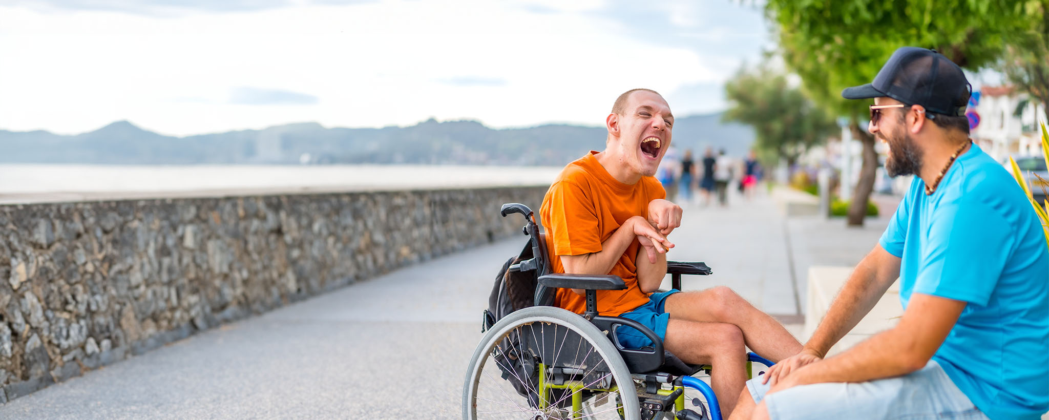 a disabled man in a wheelchair with his caregiver sitting by the beach