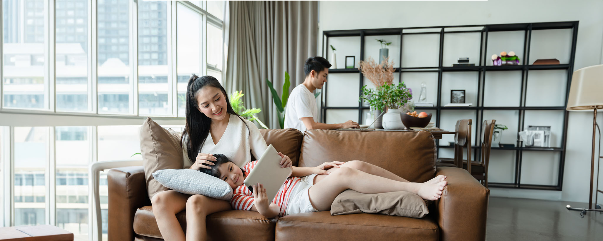 An Asian American family sitting in their living room, the daughter looks at a tablet. 