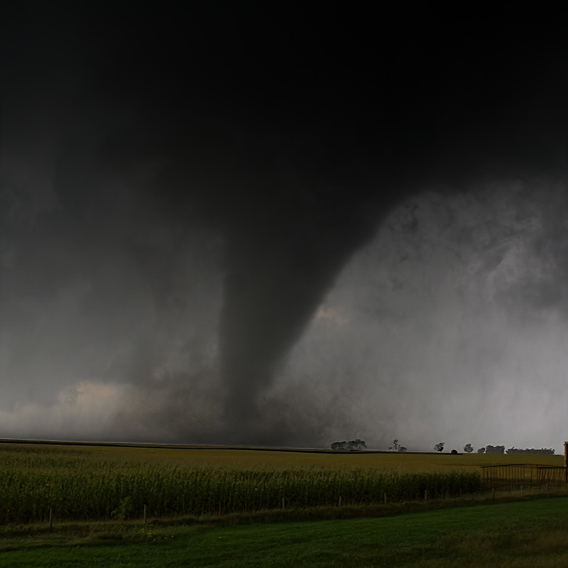 a tornado in the background of a farm with lots of fields. 