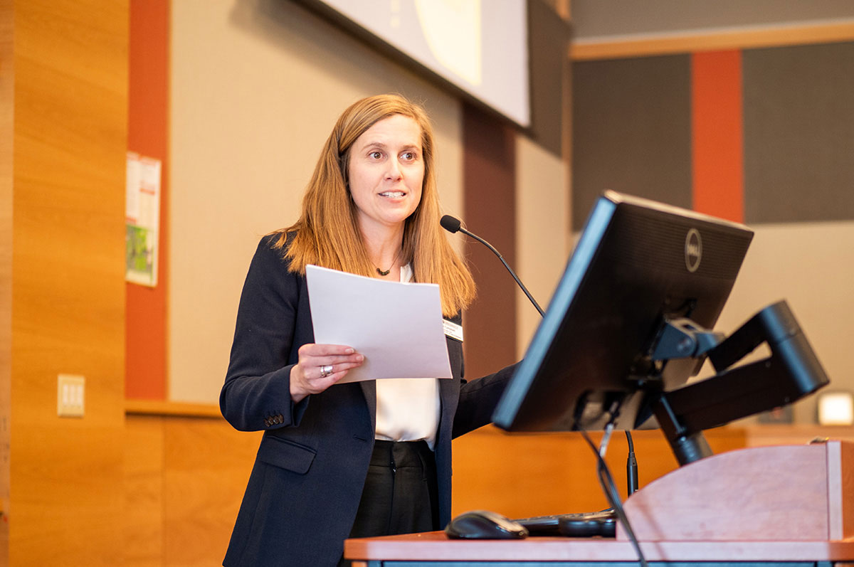 Rose Campell speaks into a microphone while presenting at a podium during a stories from wartime event