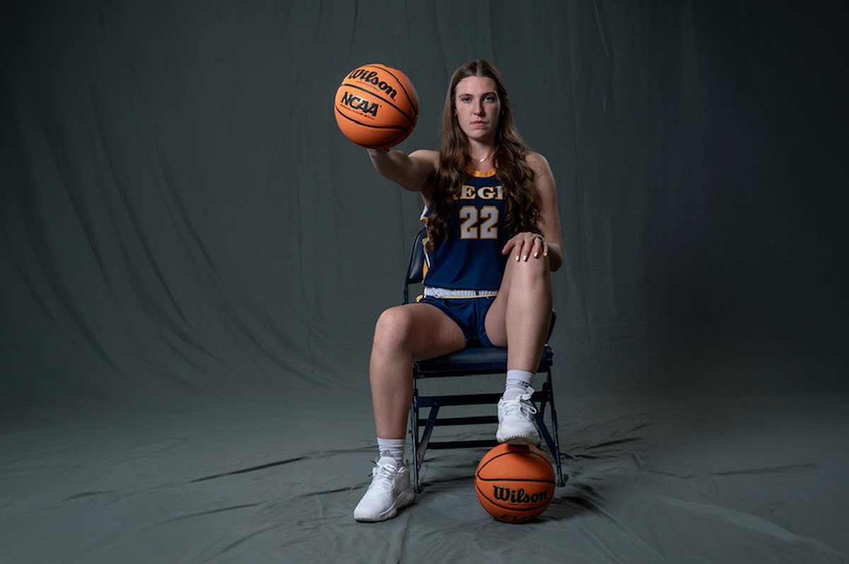 Sam Deem poses for a portrait holding a basketball in her right hand with her left foot propped on another ball