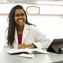 Female medical student in white coat laughs in lecture hall.