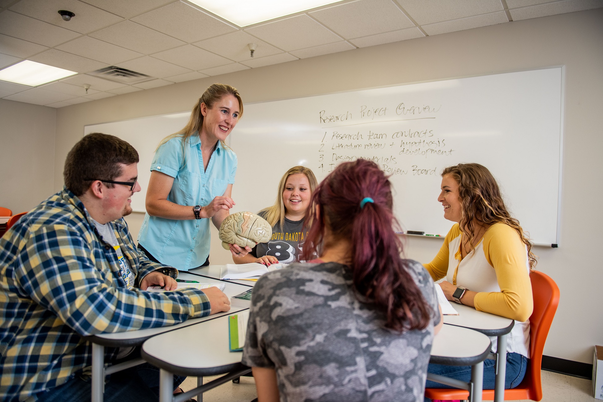 Students sitting at a table as professor talks to them in class.