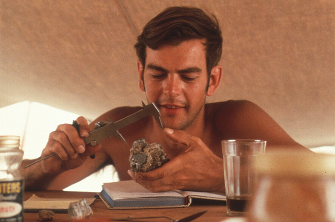 A shirtless man measures a rock mound