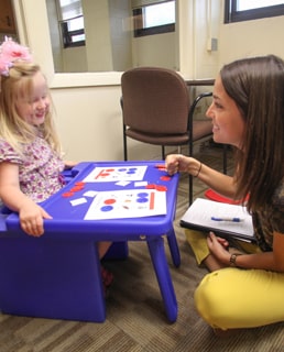 Speech therapy in session, therapist sitting on the floor with a little girl