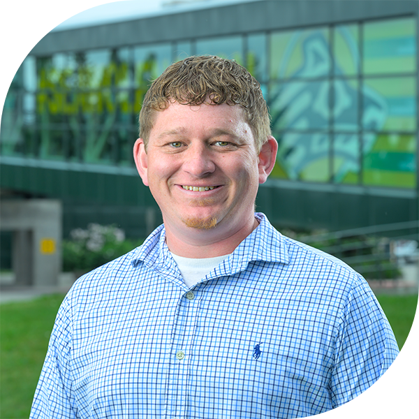 Admissions Counselor Casey Karn smiling at camera in front of Welcome to UAA kiosk.