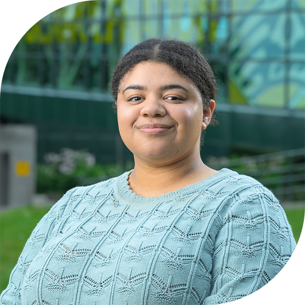 Coordinator Morrigan Kellen smiling at camera in front of Welcome to UAA kiosk.