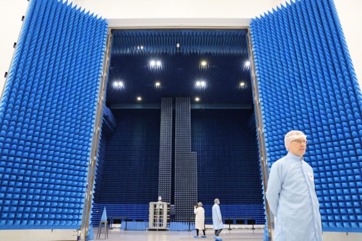 Researchers standing by a large blue structure, the National Satellite Test Facility.