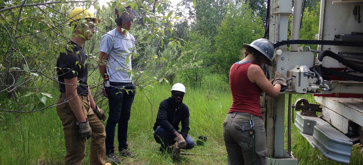 students stand around a drill bit being inserted into the earth.