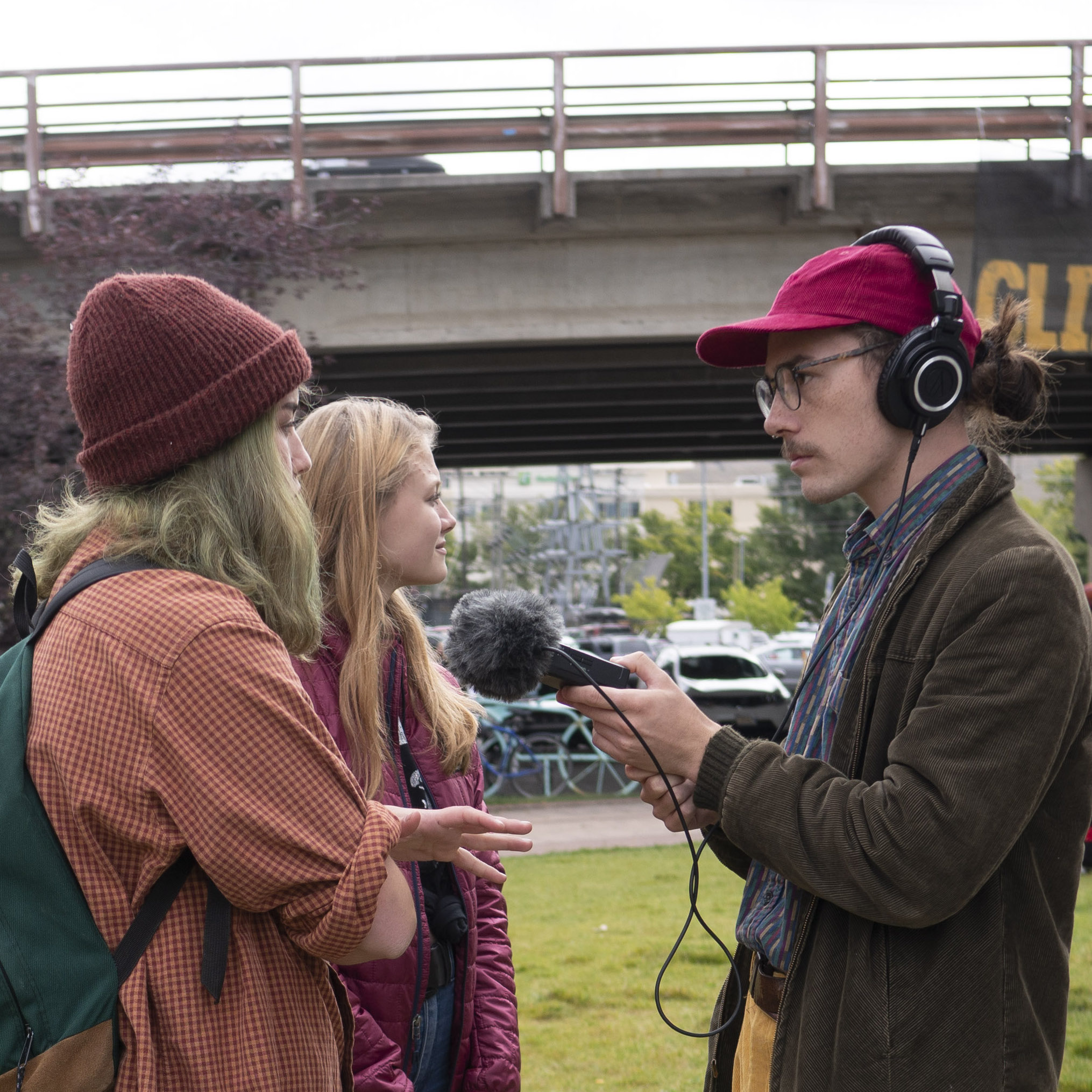 Man with microphone interviews woman in stocking cap outside.