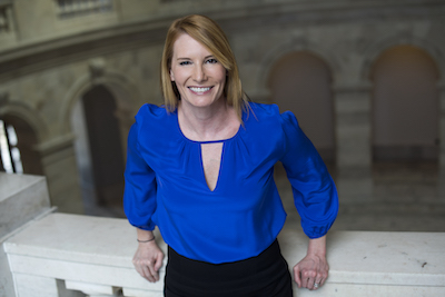 Woman in dark blue shirt stands in front of marble building.