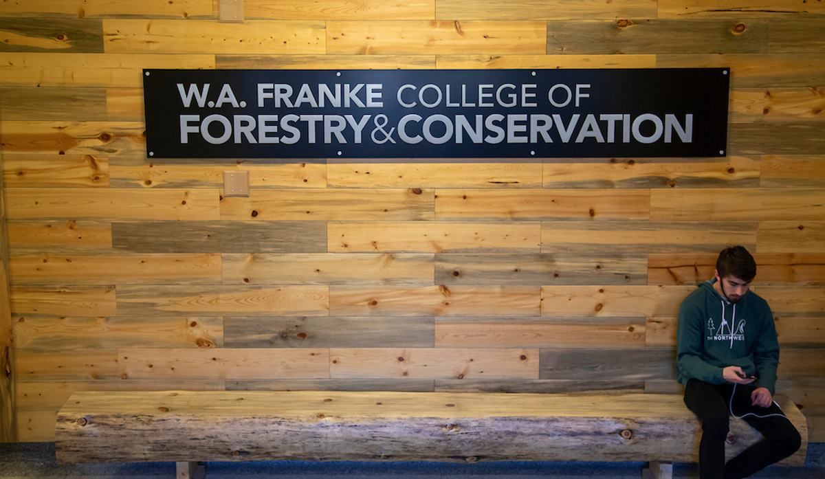 a student sits under a sign that reads W.A. Franke College of Forestry and Conservation