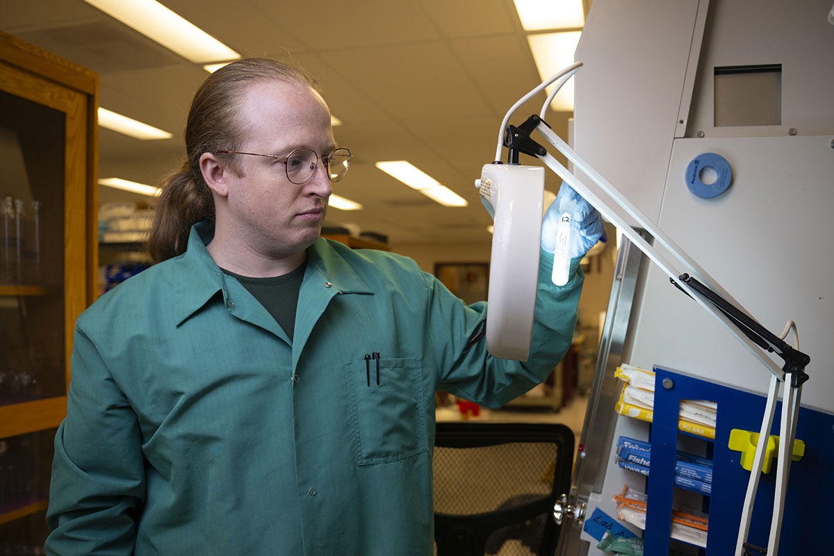 Research associate Alexander Riffey holds up a glowing test tube.