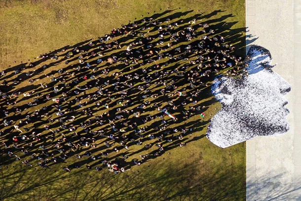 An art installation of a woman’s face with people’s shadows as her hair, seen from above.