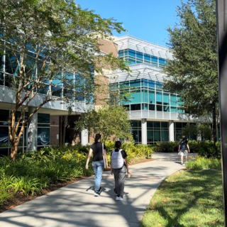 Two students walk in front of a big blue building on campus