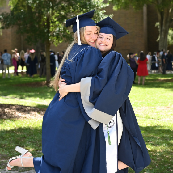 Two graduating students in caps and gowns smile and hug