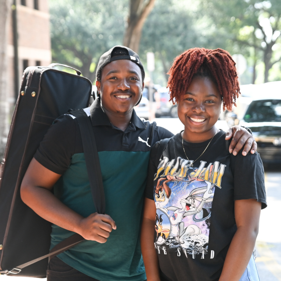 Two students smile at the camera, one student has a backpack on