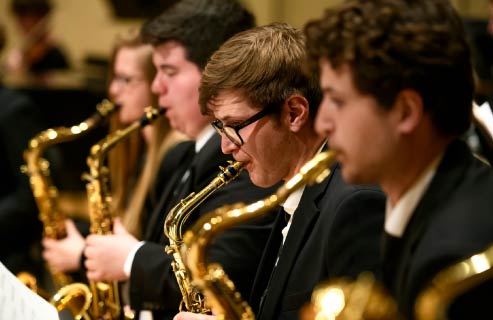 A photo of four UW saxaphone players dressed in black tuxedos playing at concert.