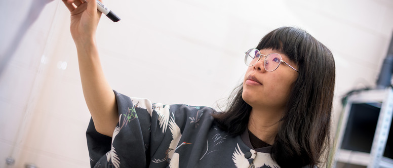 student wearing glasses writing on a white board