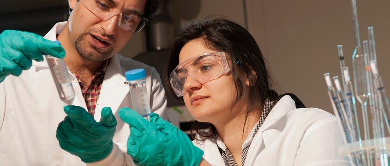 Two students conduct an experiment with green gloves on.