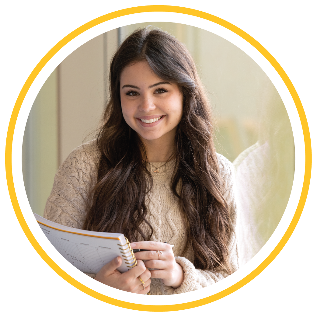 female student smiling at the camera and holding a planner