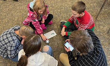 children sitting in a circle on the floor playing with a ball-shaped device